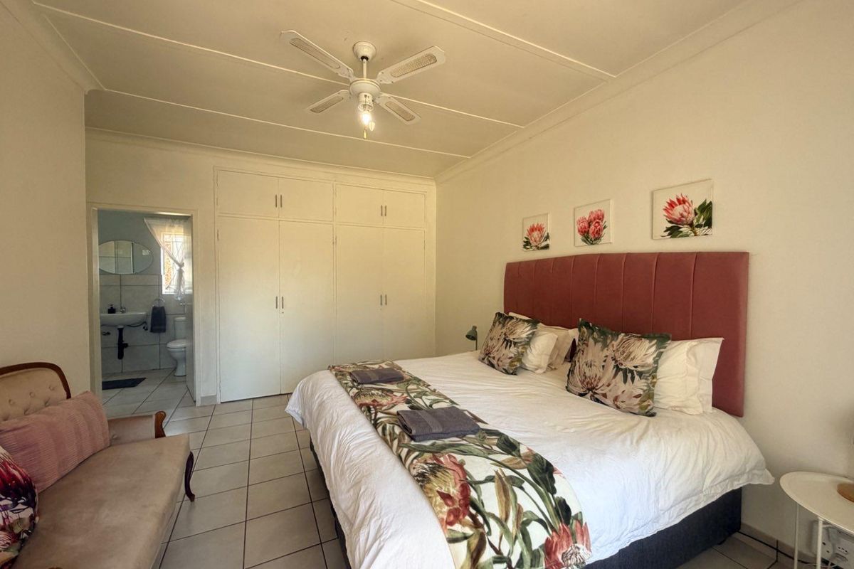Spacious bedroom featuring built-in cupboards, tiled flooring, a ceiling fan, and direct access to an en-suite bathroom.