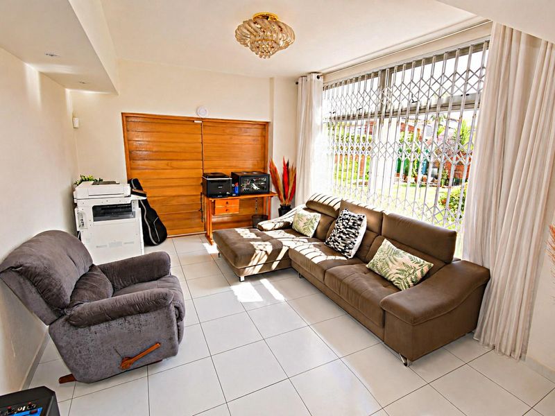 A bright living room featuring tiled flooring, a large window with a security gate, and a sliding door leading to the exterior.