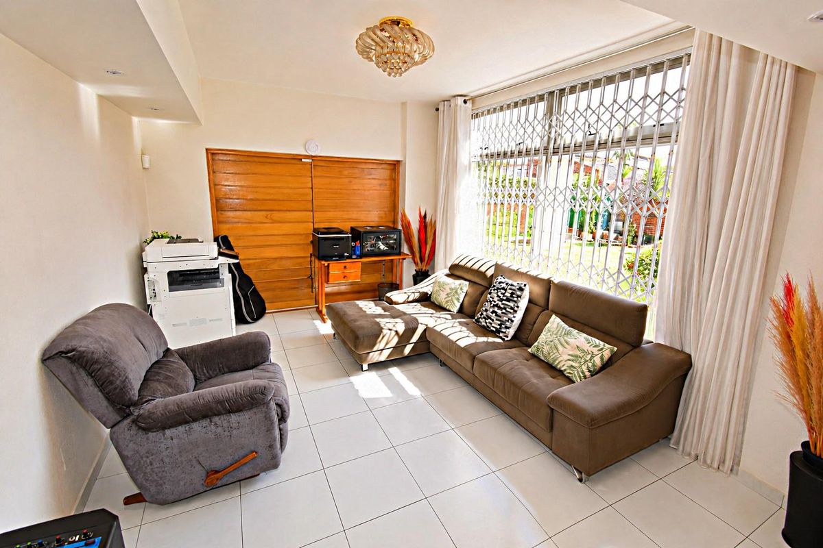 A bright living room featuring tiled flooring, a large window with a security gate, and a sliding door leading to the exterior.