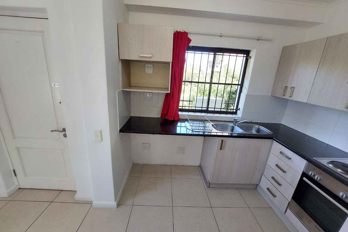 A functional kitchen featuring light wood-tone cabinetry, dark granite countertops, a built-in oven, and tiled flooring with security bars on the window.
