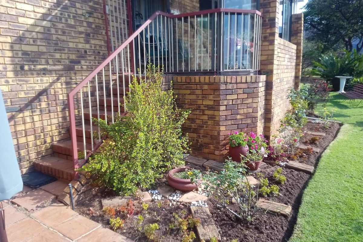 A view of the exterior rear garden area featuring a brick facade, raised patio steps with metal railings, and landscaped garden beds.
