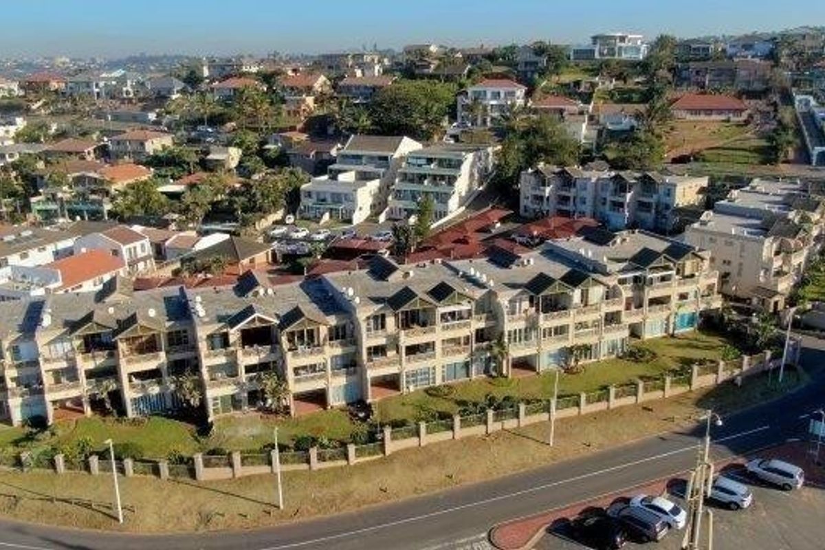 An aerial view of a residential apartment complex featuring multiple units with balconies, tiled roofs, and a perimeter wall, situated in a suburban neighborhood.