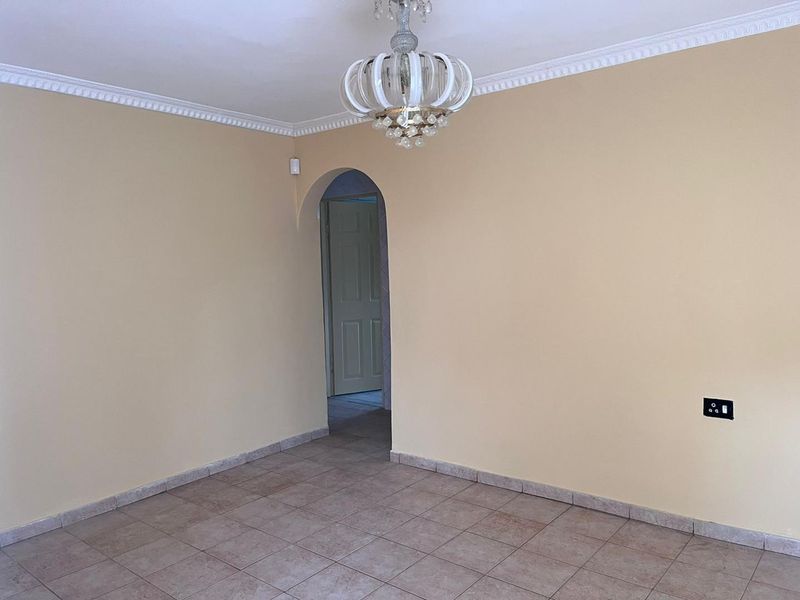An empty living room featuring ceramic tile flooring, decorative crown molding, and an arched doorway leading to an adjacent space.
