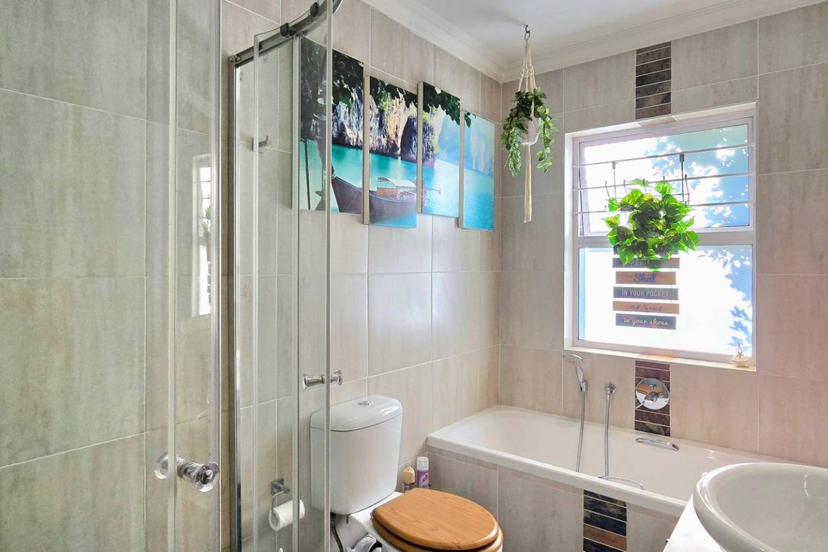 A well-maintained bathroom featuring a shower enclosure, bathtub, toilet, and washbasin with neutral wall tiling and natural light from a window.