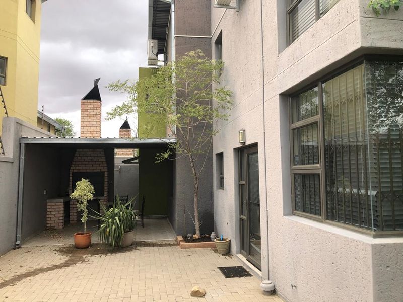 Rear exterior view of the townhouse featuring a paved patio area with a built-in brick braai and covered entertainment space.