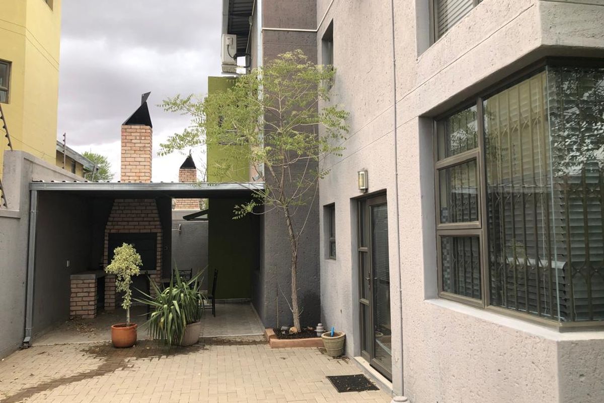 Rear exterior view of the townhouse featuring a paved patio area with a built-in brick braai and covered entertainment space.