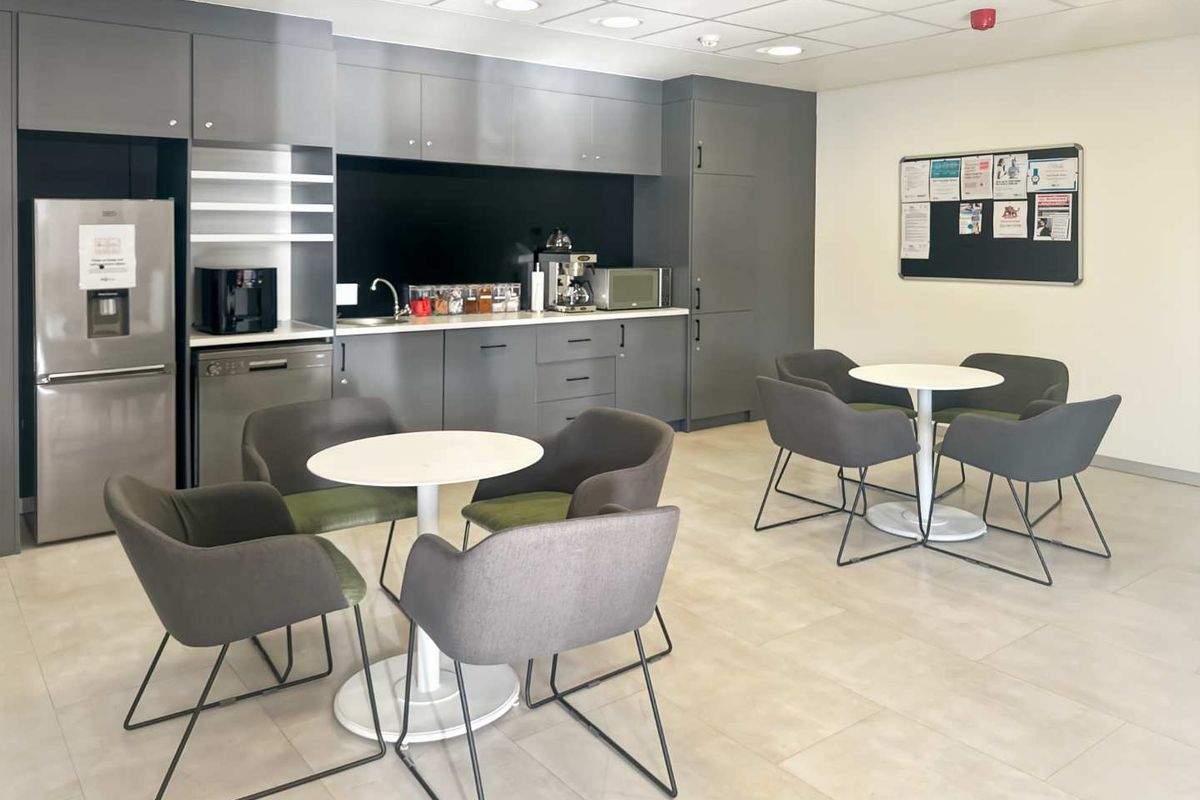 A modern office kitchenette featuring sleek grey cabinetry, integrated storage, a stainless steel sink, and a clean tiled floor.