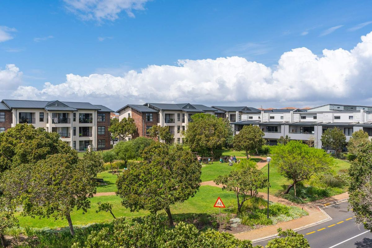 An elevated aerial view of the apartment complex grounds, featuring well-maintained communal gardens, paved pathways, and surrounding residential buildings.
