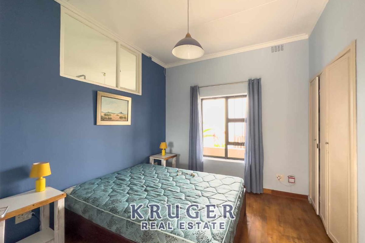 A bedroom featuring wooden flooring, built-in cupboards, and a high-level interior window providing additional natural light.