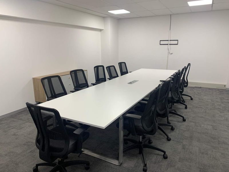 A functional office meeting room featuring a large central table, carpeted flooring, and recessed ceiling lighting.