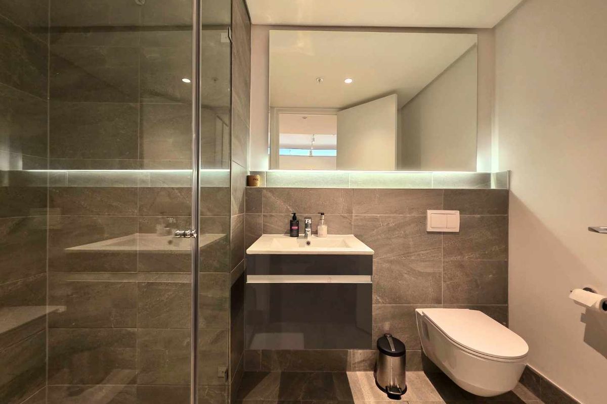 Modern bathroom featuring a glass-enclosed shower, wall-mounted vanity with integrated basin, wall-hung toilet, and contemporary tiled finishes with ambient LED lighting.