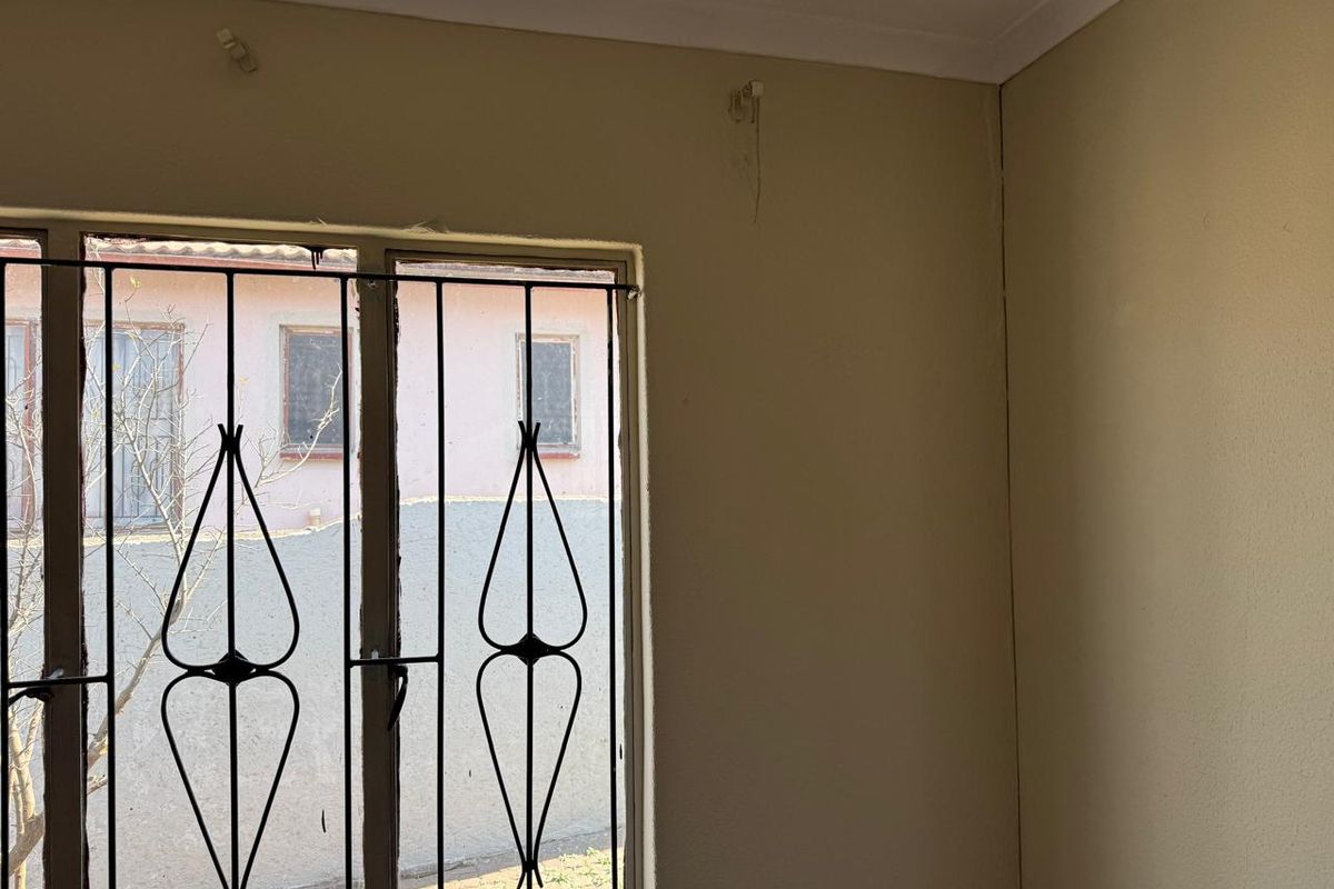 A bedroom interior featuring security bars on the window, showing visible wall cracks and signs of wear requiring maintenance and cosmetic repair.