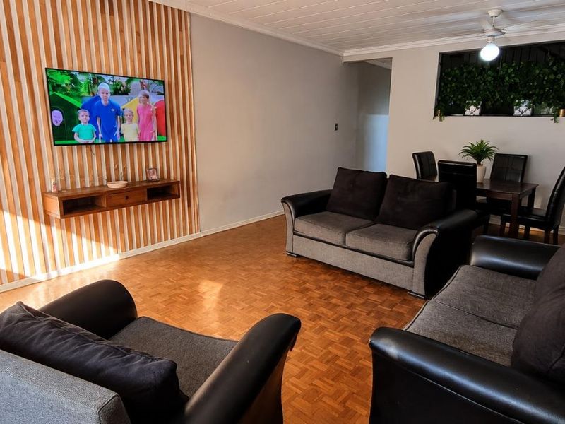 An open-plan living and dining area featuring warm parquet flooring, a decorative timber slat feature wall, and a ceiling fan.