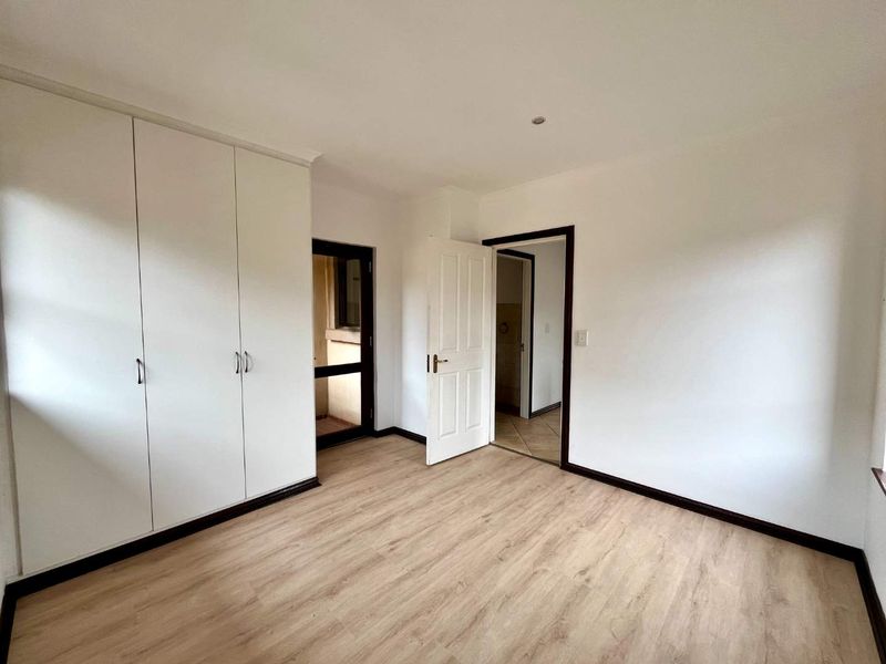 A bright, empty bedroom featuring light-toned laminate flooring, built-in cupboards, and direct access to an external area.