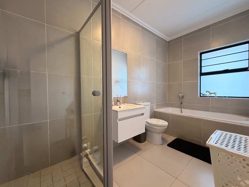 Modern bathroom featuring a walk-in shower with glass enclosure, a built-in bathtub, and a wall-mounted vanity with neutral floor-to-ceiling tiling.