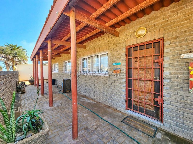 A covered patio area featuring brick walls, a wooden pergola structure, and a security gate entrance, providing a functional outdoor space.