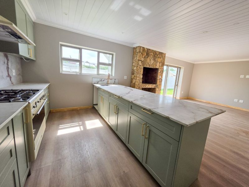 Modern open-plan kitchen featuring sage green cabinetry, marble-look countertops, gas hob, and a striking stone-clad fireplace in the adjacent living area.
