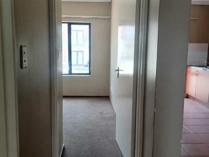 A view from the hallway looking into an empty bedroom, with tiled flooring and an archway leading to the kitchen area.