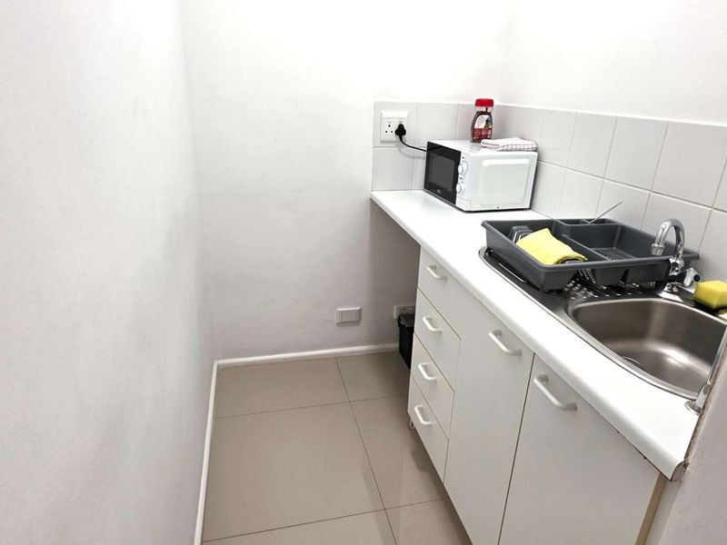 A compact scullery area featuring built-in white cabinetry, a stainless steel sink, and tiled backsplash, providing functional utility space.