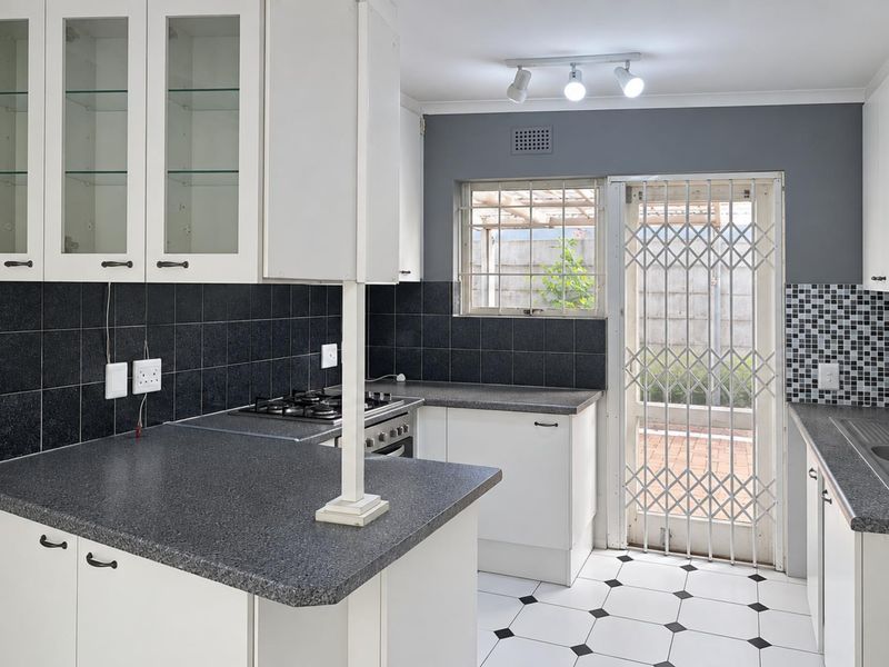 A clean, functional kitchen featuring white cabinetry, dark laminate countertops, a gas hob, and tiled flooring with direct access to the rear exterior.