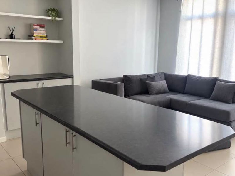 Modern open-plan living area featuring a central kitchen island with dark countertops, light grey cabinetry, and built-in floating shelving.