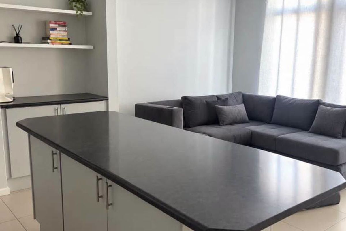 Modern open-plan living area featuring a central kitchen island with dark countertops, light grey cabinetry, and built-in floating shelving.
