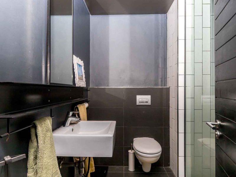 Modern bathroom featuring a wall-mounted basin, wall-hung toilet with concealed cistern, and a tiled shower enclosure with dark contemporary finishes.