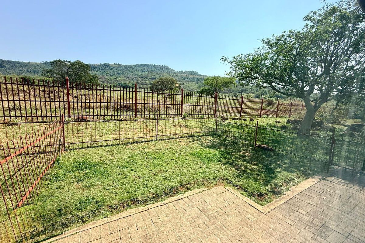 A private rear garden featuring a paved patio area, lawn, and metal perimeter fencing with scenic mountain views.