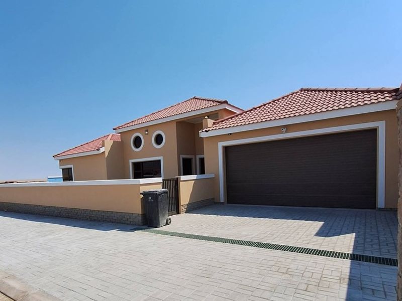 Front elevation of a modern house featuring a double garage, paved driveway, and perimeter boundary wall under a clear sky.