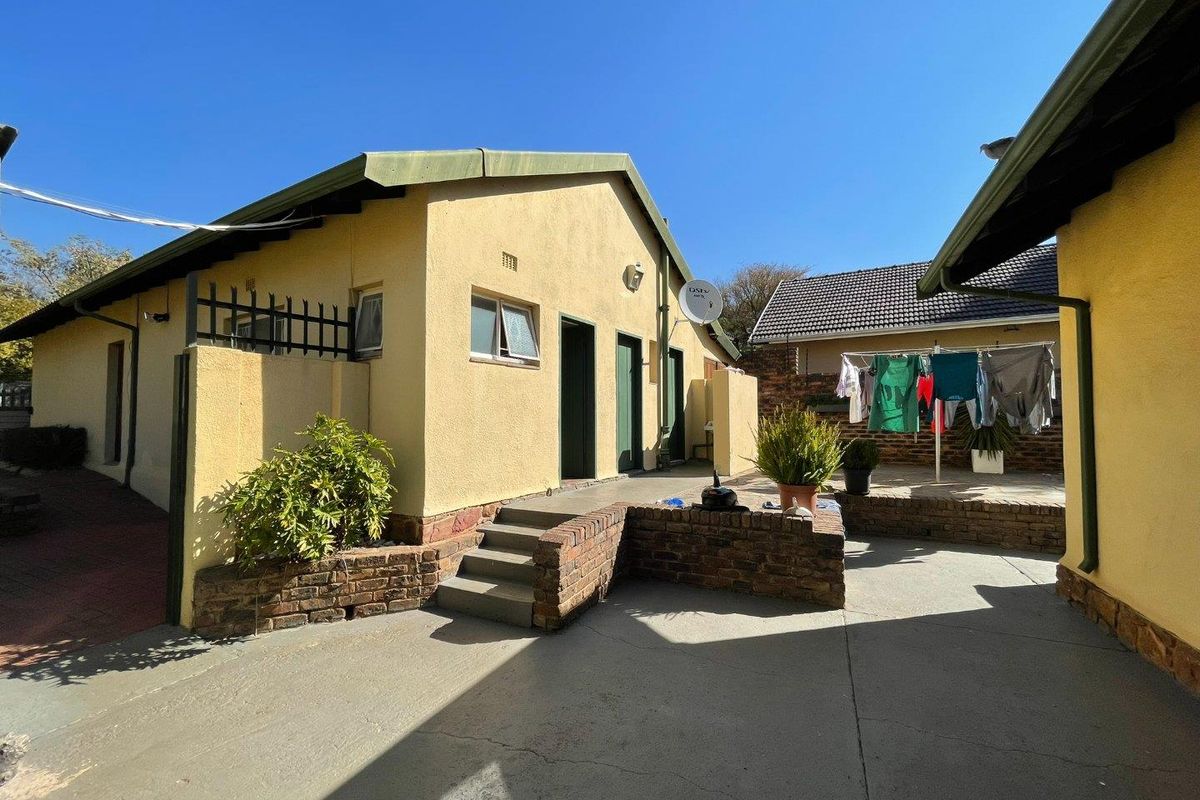 Rear exterior view of the property featuring a paved courtyard, brick retaining walls, and access to the main building structure.