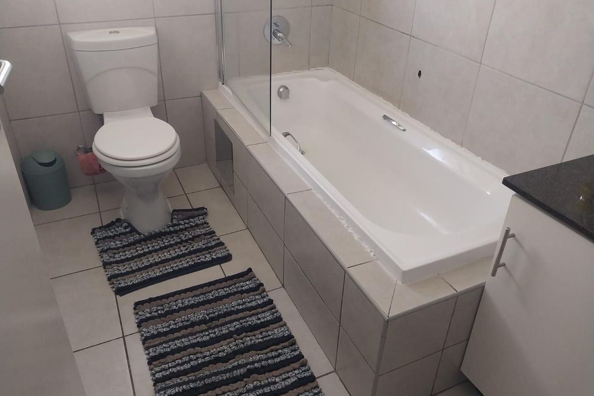 A functional bathroom featuring a built-in bathtub with a glass shower screen, a toilet, and a vanity cabinet with a granite countertop.