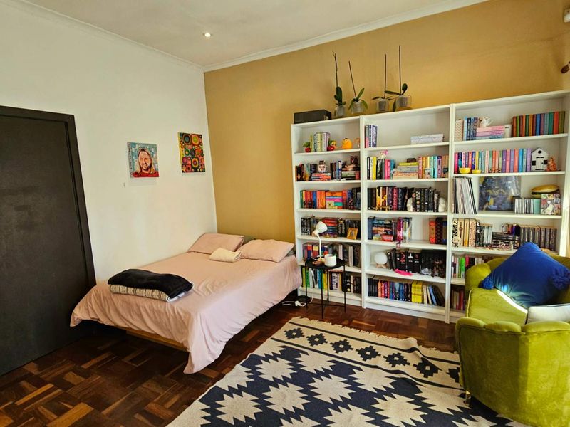 A bedroom featuring classic parquet flooring and a large built-in floor-to-ceiling shelving unit, providing ample storage space.