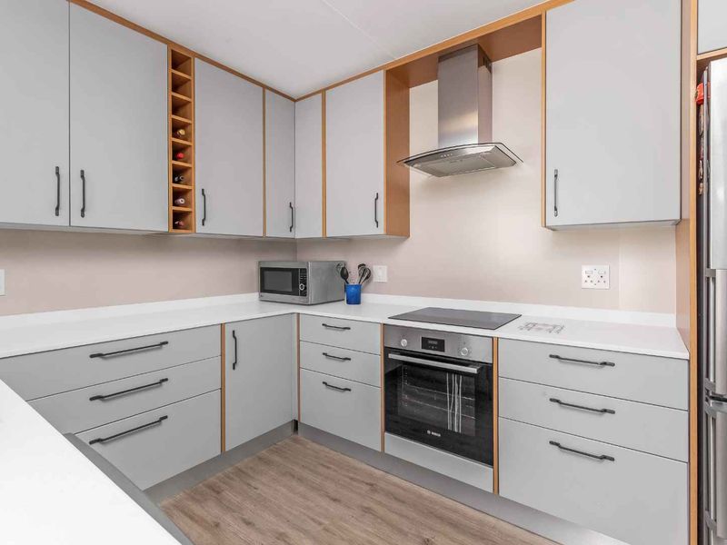 A modern, well-maintained kitchen featuring light grey cabinetry, integrated appliances including an oven and hob, and durable laminate flooring.