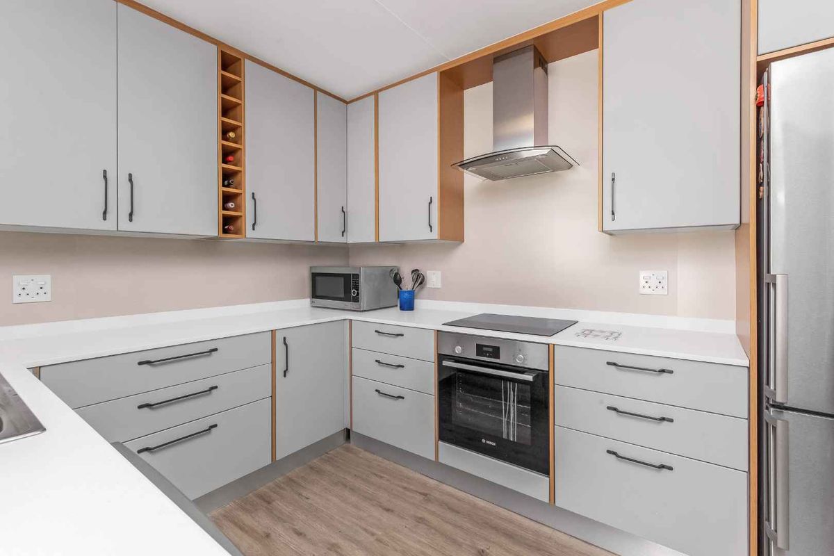A modern, well-maintained kitchen featuring light grey cabinetry, integrated appliances including an oven and hob, and durable laminate flooring.