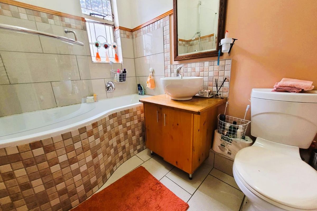 A functional bathroom featuring a bathtub with shower mixer, a vessel sink vanity, and a standard toilet with tiled wall accents.