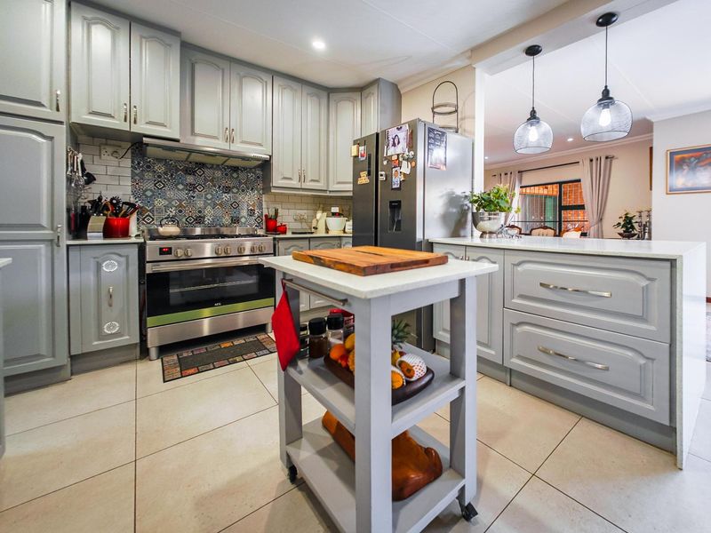 A well-maintained kitchen featuring grey cabinetry, a gas stove with a decorative tiled backsplash, and a central island with pendant lighting.