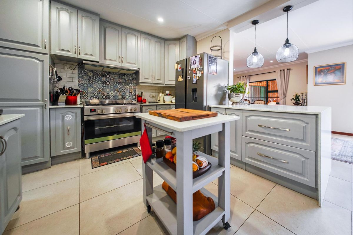 A well-maintained kitchen featuring grey cabinetry, a gas stove with a decorative tiled backsplash, and a central island with pendant lighting.