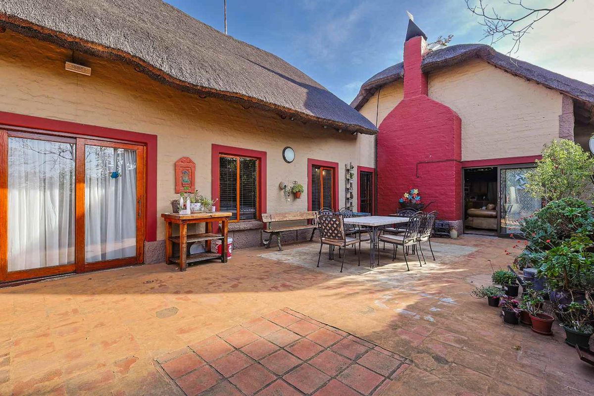 A rear courtyard featuring a traditional thatched roof, brick chimney, and paved patio area with direct access to the home through sliding glass doors.