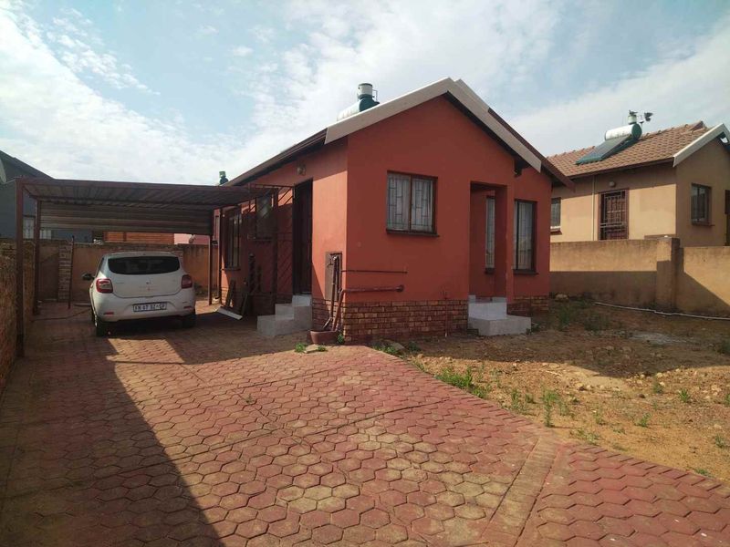 Front view of a detached house featuring a paved driveway, attached carport, solar water heater, and secure perimeter walling.