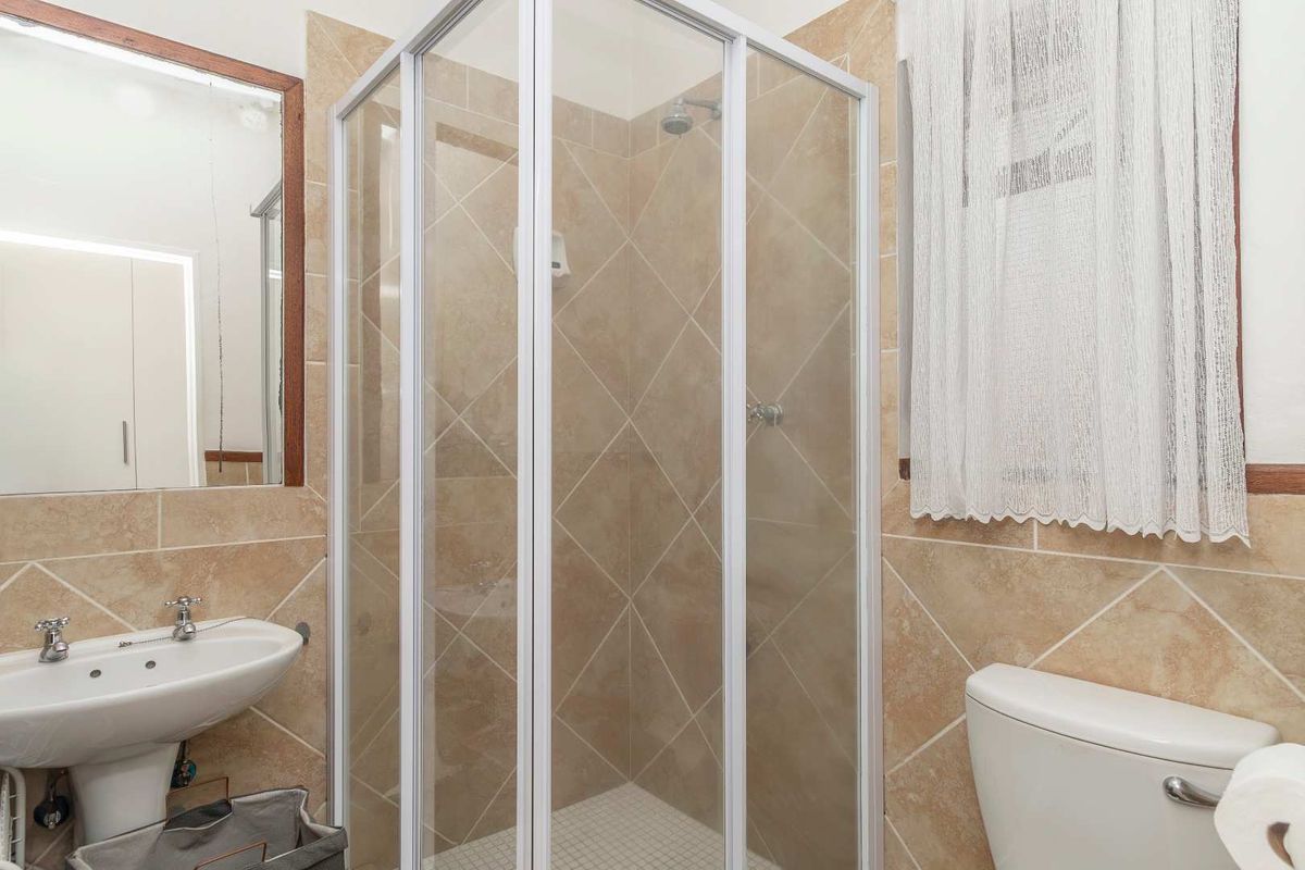 A functional bathroom featuring a corner shower enclosure, pedestal basin, and toilet with neutral wall tiling.