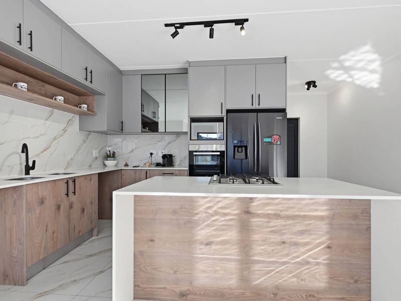 Modern kitchen featuring two-tone cabinetry, marble-look splashback, central island with gas hob, and high-end built-in appliances.