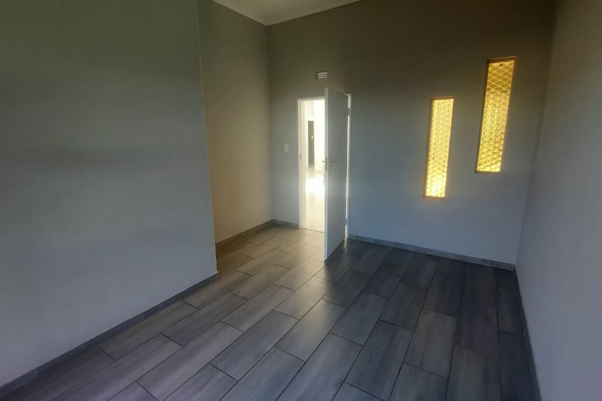 A bright, empty room featuring modern wood-look floor tiles and unique vertical decorative glass wall inserts.