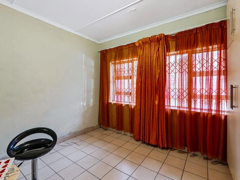 A bedroom featuring tiled flooring, built-in cupboards, and security bars on the windows, requiring some cosmetic updates to the wall finishes.