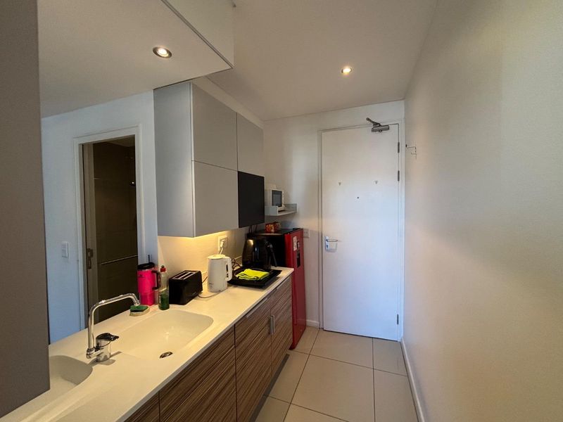 Compact kitchen area featuring modern cabinetry, integrated sink, and tiled flooring, adjacent to the main apartment entrance.