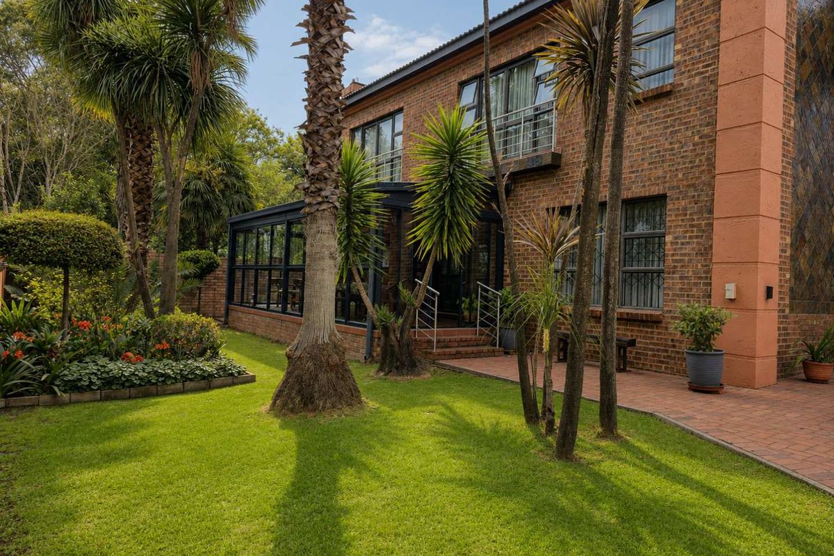 Rear view of a double-storey face brick house featuring a landscaped garden, paved walkway, covered patio area, and upper-level balcony.