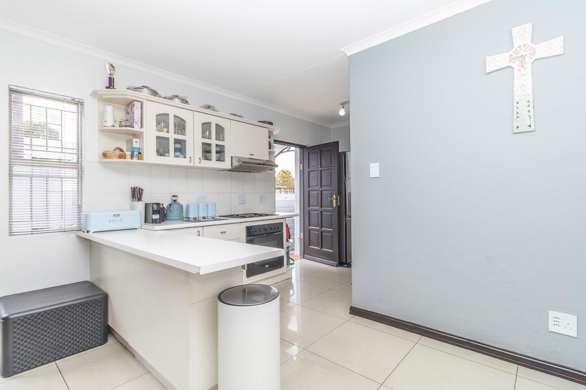 A functional kitchen featuring built-in cabinetry, a breakfast counter, integrated oven and hob, and tiled flooring with direct access to the exterior.