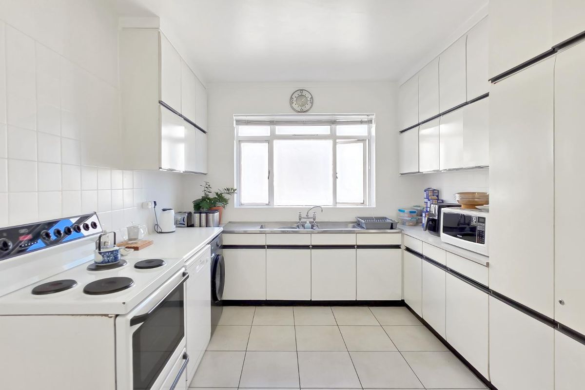 A functional galley-style kitchen featuring white cabinetry, tiled flooring, a built-in electric stove, and a stainless steel sink under a window.
