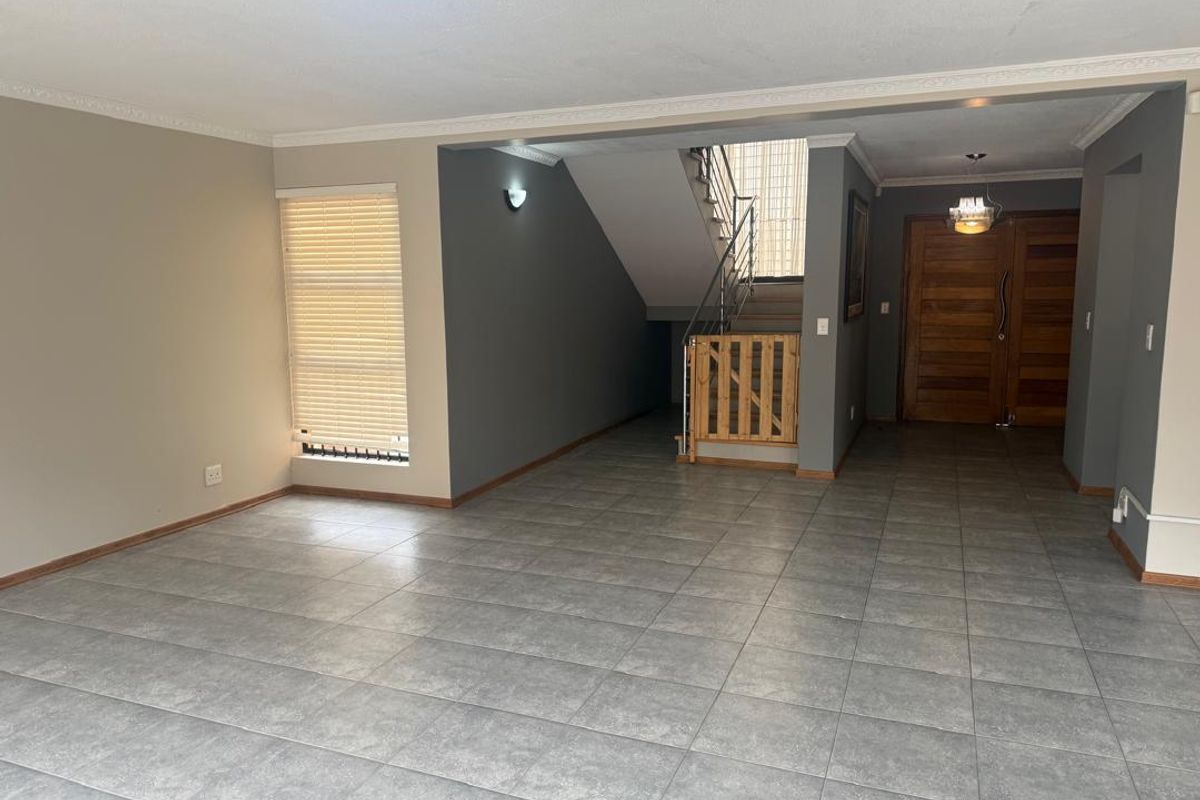 Spacious open-plan living area featuring neutral walls, large tiled flooring, and a staircase with a modern metal balustrade leading to the upper level.