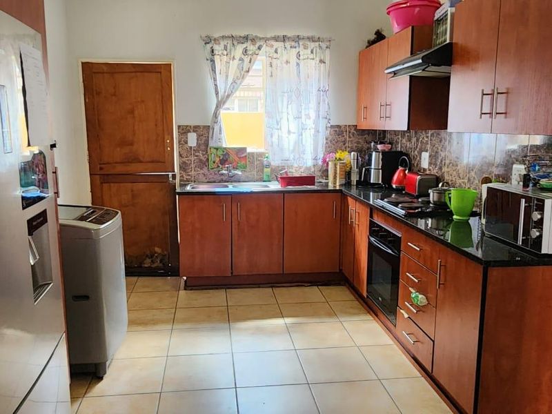A functional kitchen featuring wooden cabinetry, granite countertops, a built-in oven, hob, extractor fan, and tiled flooring with a rear access door.