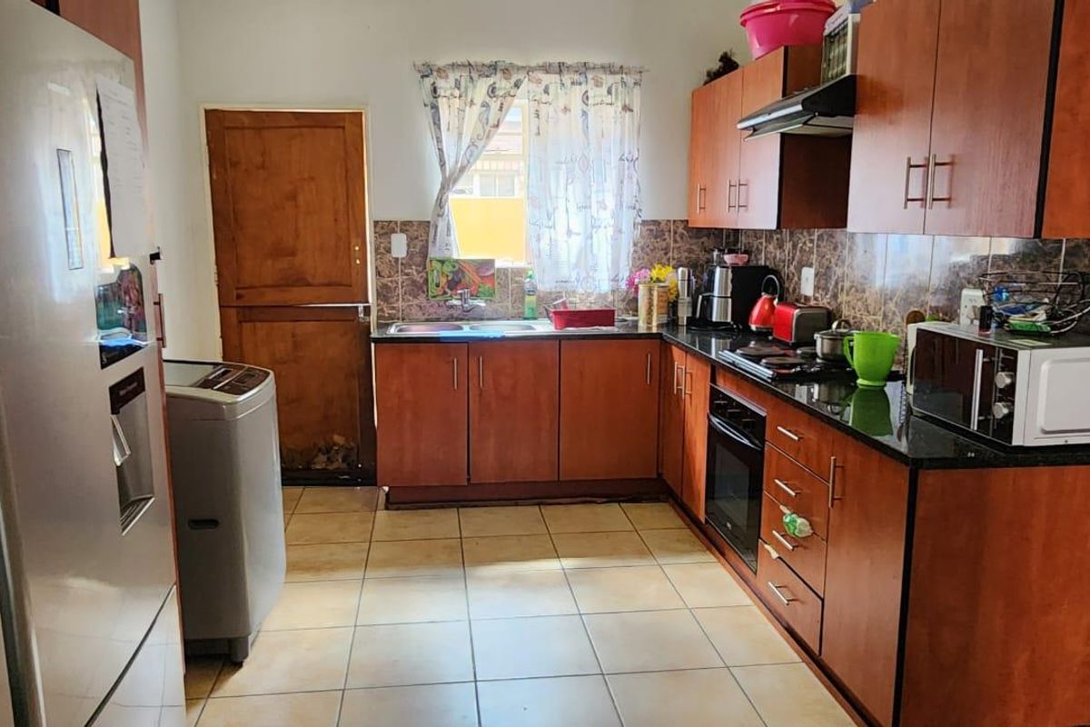 A functional kitchen featuring wooden cabinetry, granite countertops, a built-in oven, hob, extractor fan, and tiled flooring with a rear access door.